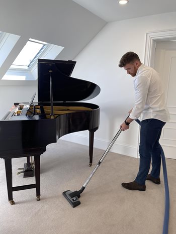 Beam Vacuum cleaning around piano in hallway