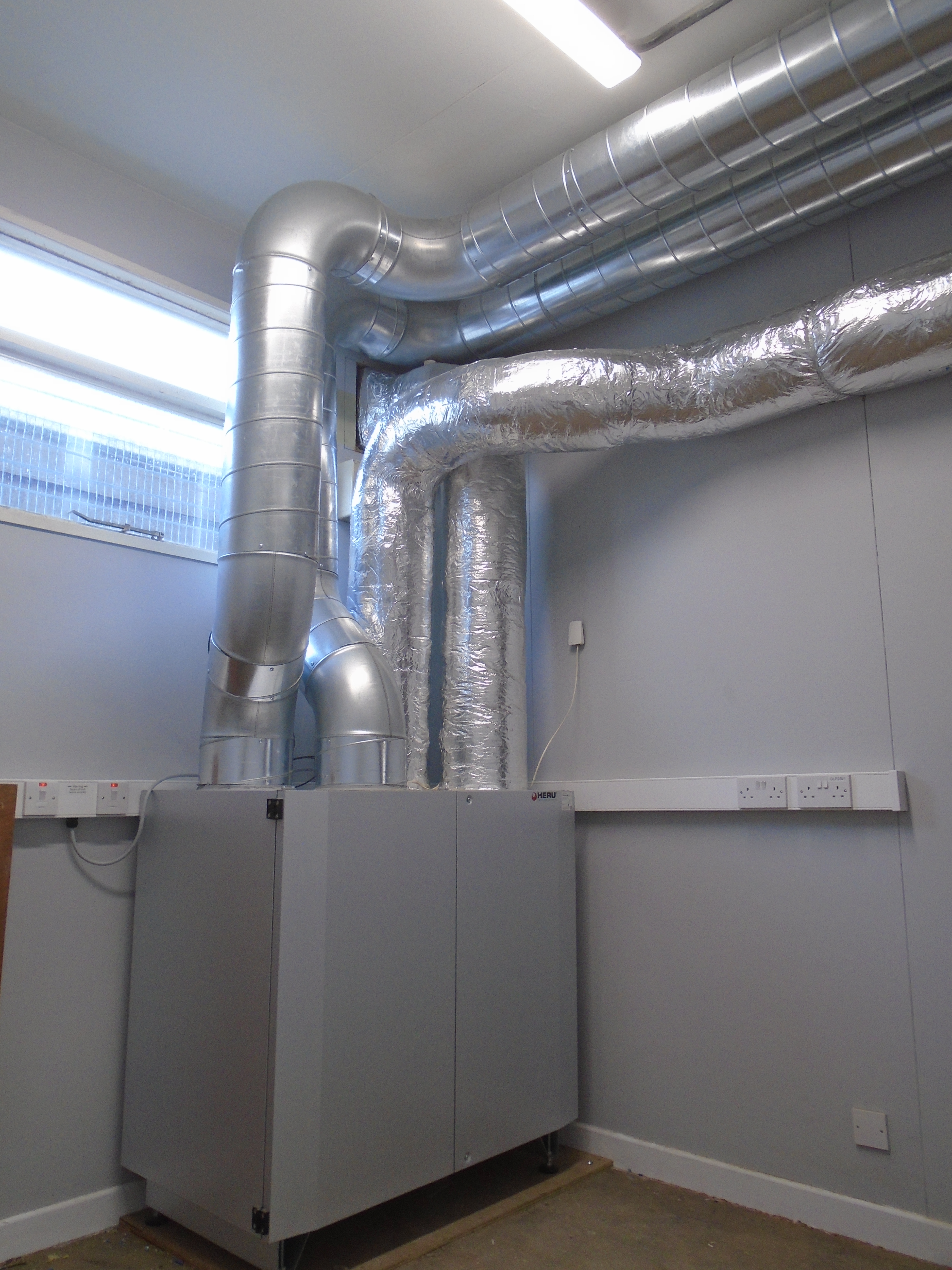 Beam MVHR unit with insulated ductwork running along laboratory ceiling