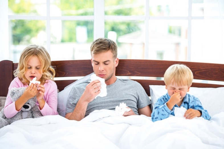 Dad and children sneezing in bed with allergies